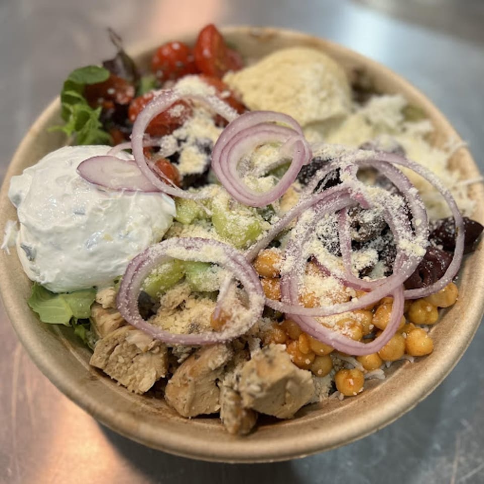 A colorful salad bowl from Poppy's Place, featuring chicken, chickpeas, tomatoes, onions, and creamy dressing.