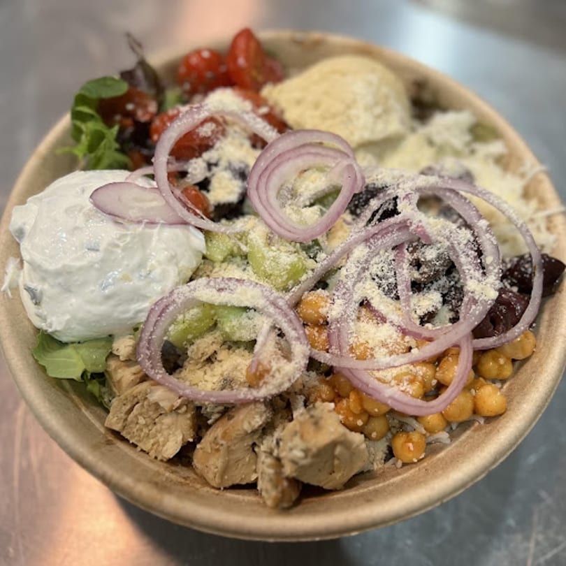 A colorful salad bowl from Poppy's Place, featuring chicken, chickpeas, tomatoes, onions, and creamy dressing.