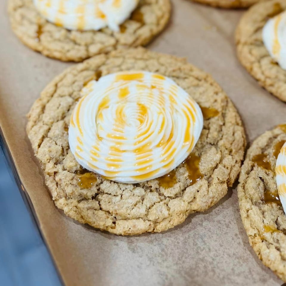 Close-up of Poppy's Place cookies with white frosting and caramel drizzle on parchment paper.
